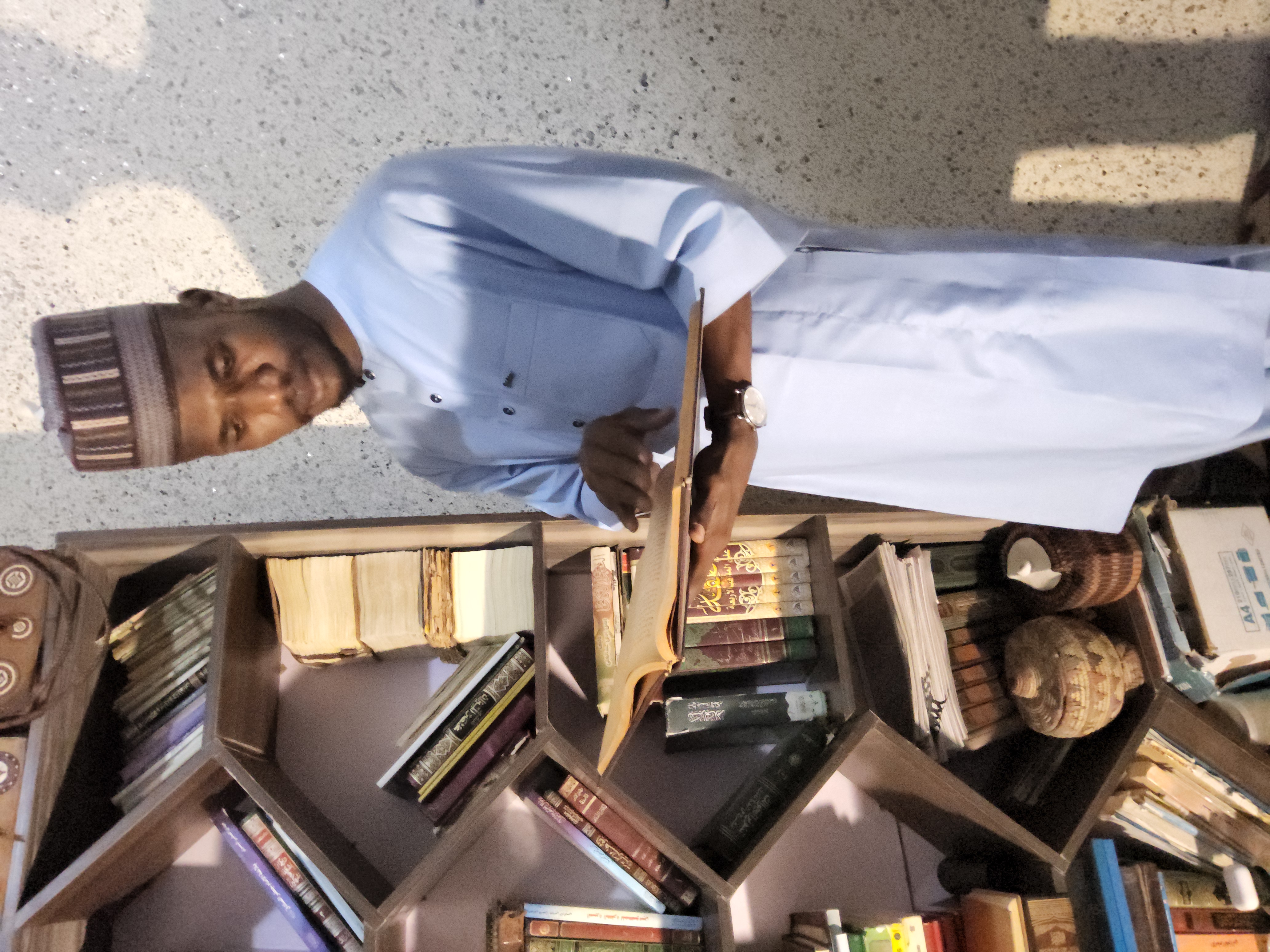 Musa Allama reading beside a bookshelf